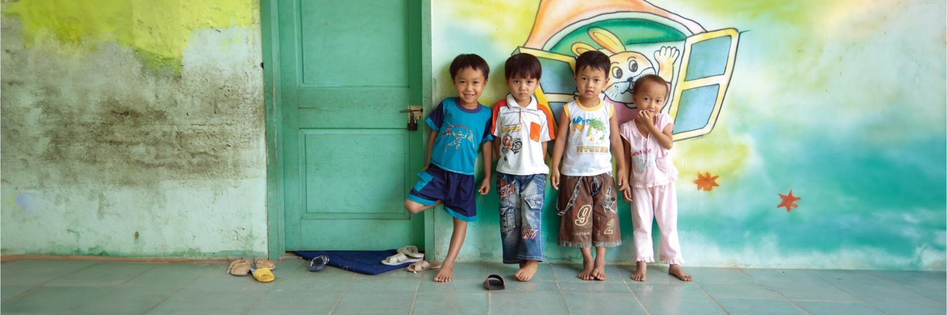 Vier kindjes staan tegen een muur met een tekening