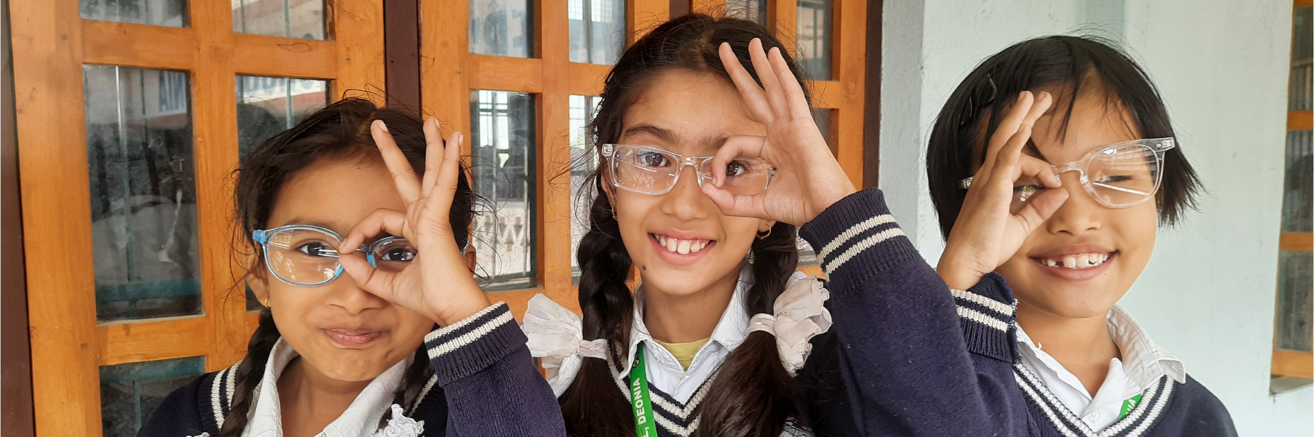 Drie meisjes in Nepal laten oogteken met hun vingers zien uit dankbaarheid voor hun nieuwe bril
